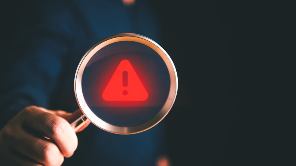 Red warning icon on a magnifying glass lens held by a hand.